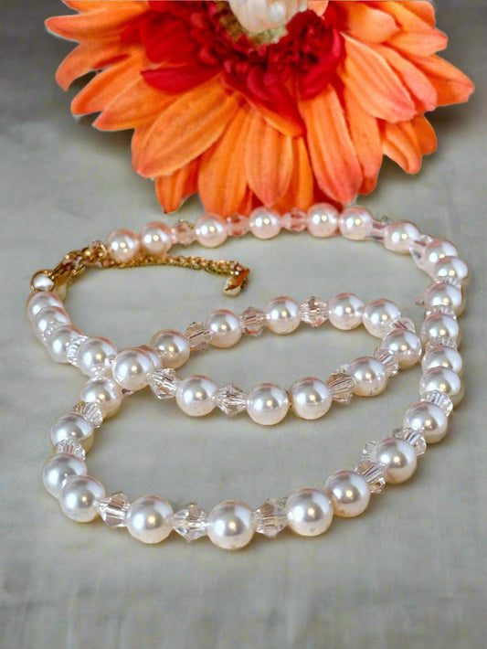 Handmade Swarovski pearl and crystal necklace with gold filled lobster clasp and extender, styled on a textured cream surface with an orange flower in the background.