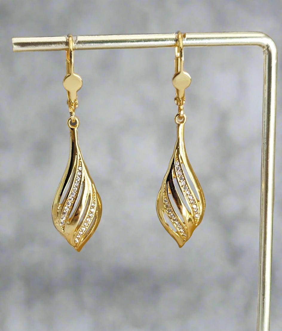 Close-up of a 14K gold plated sterling silver drop earring with a leaf-inspired design and sparkling cubic zirconia, worn on a black mannequin.