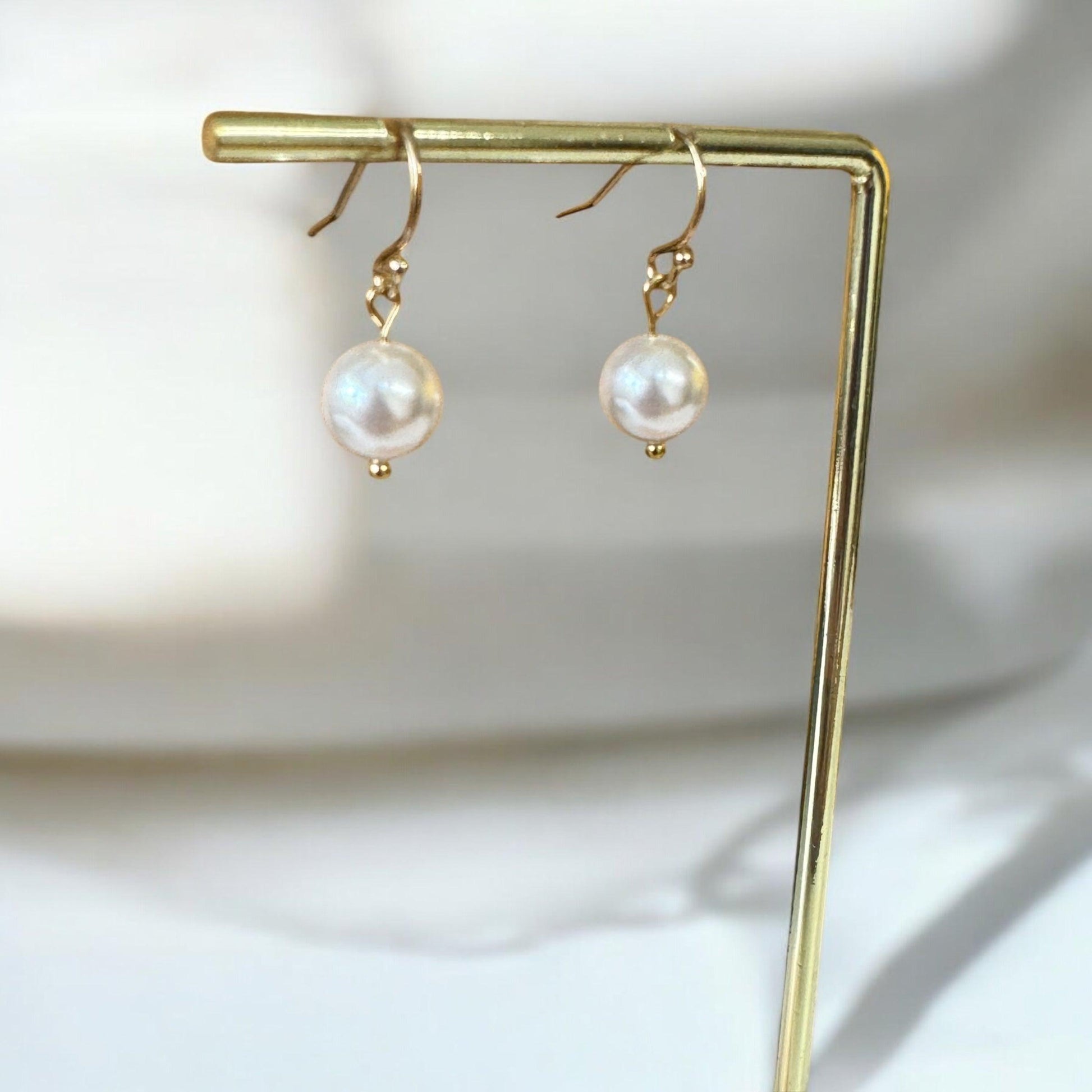 Pair of 14K gold-filled Swarovski pearl drop earrings displayed against a white ceramic background, showcasing their elegant design and lustrous pearls.