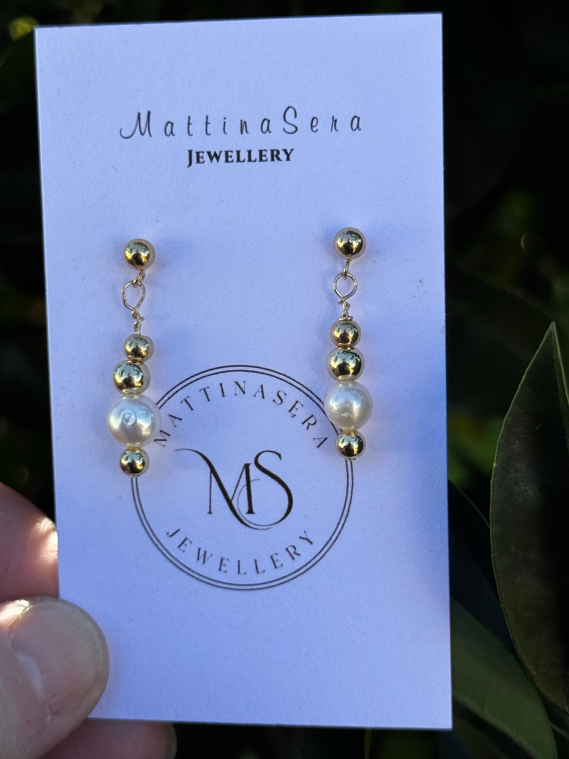 Pair of earrings on a Mattiasera Jewellery card held by a hand with a leafy background.