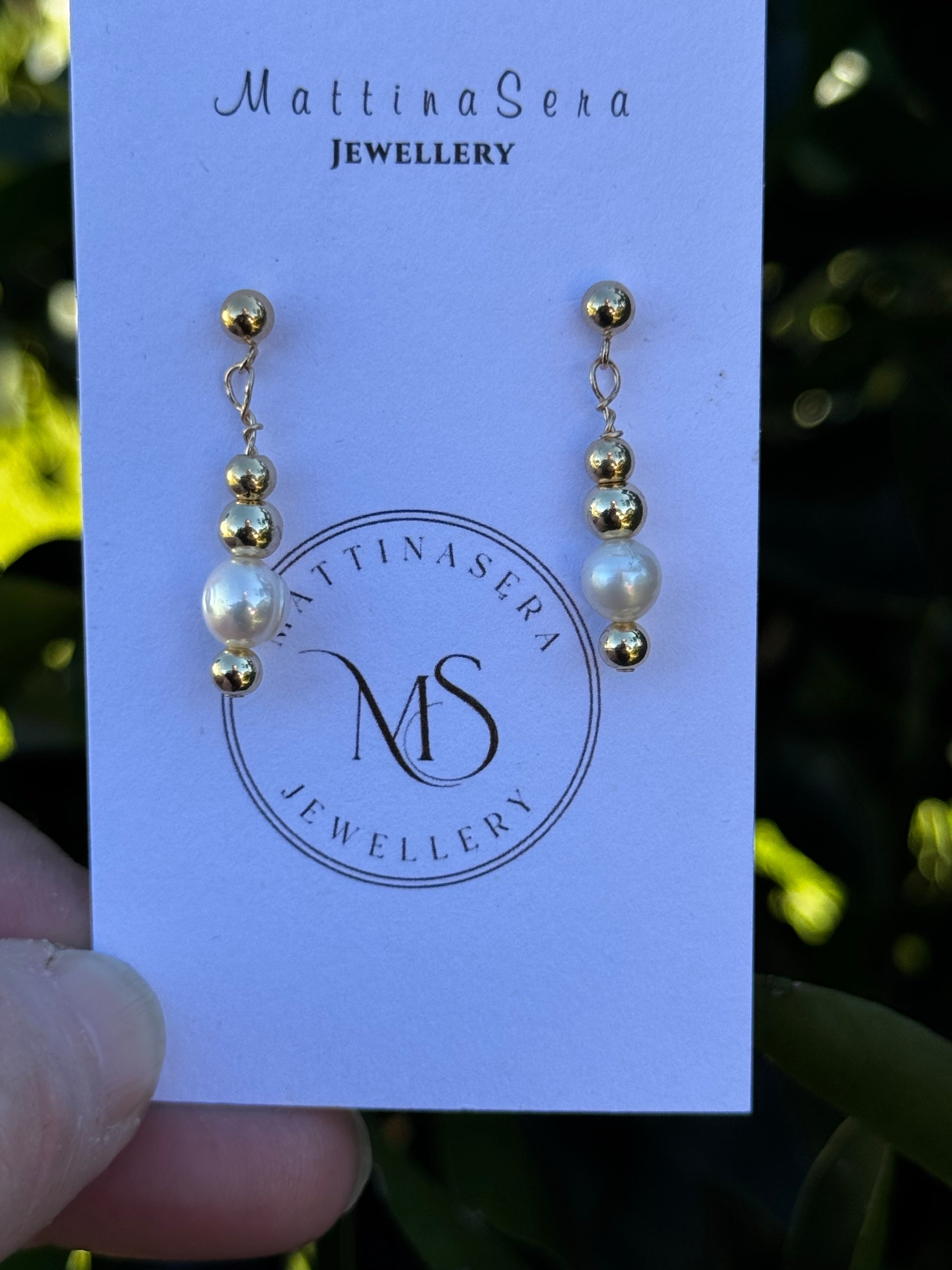 Pair of gold and pearl earrings on a MattinaSera Jewellery card.