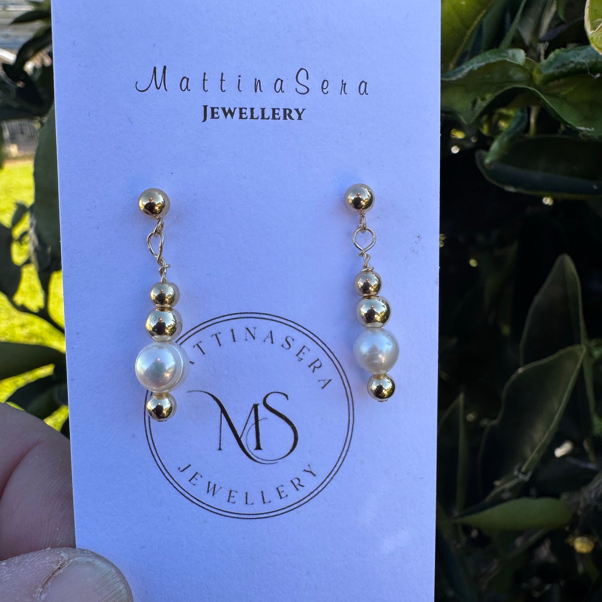 Pair of pearl earrings on a Mattina Sera Jewellery card with green foliage in the background
