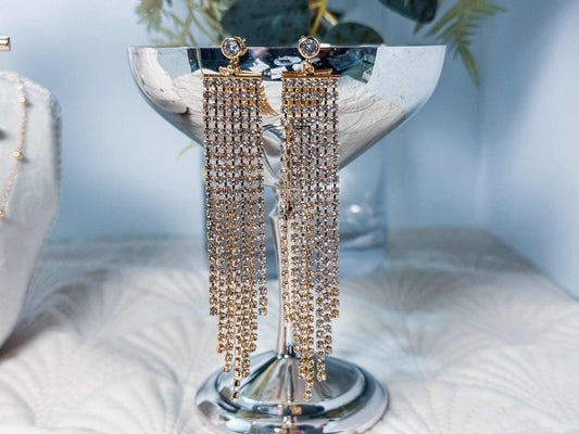 Pair of gold tassel earrings on a silver stand with a light blue background