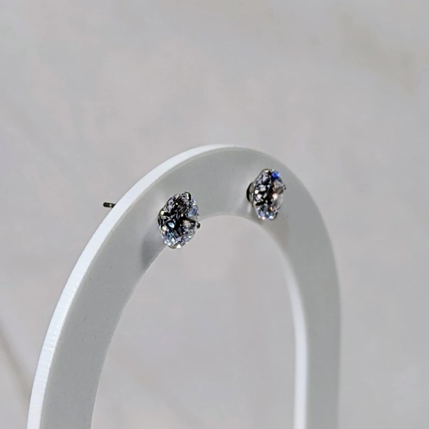 Pair of silver cubic zirconia stud earrings with gemstones on a white stand against a light grey background