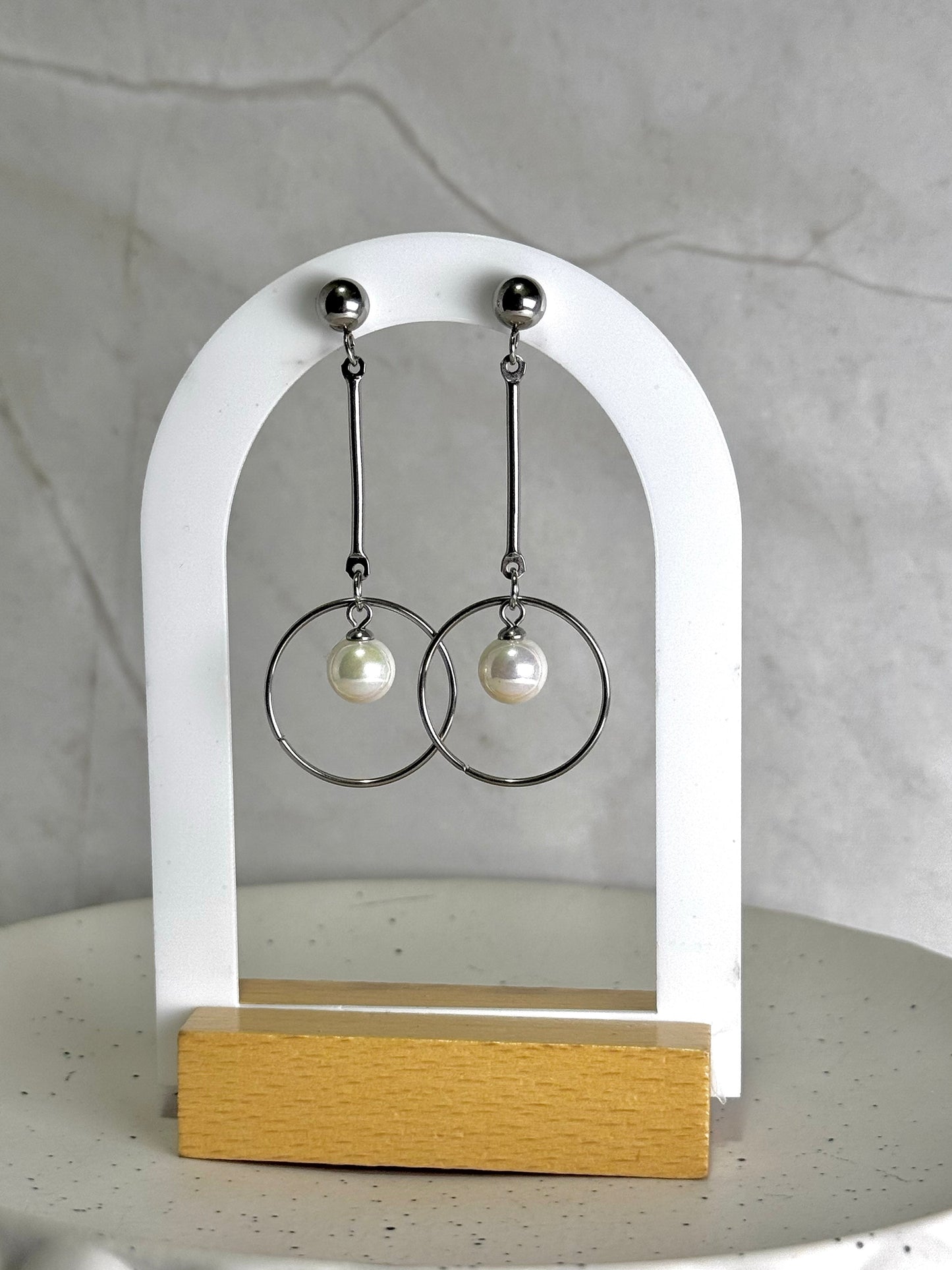 Pair of earrings on a white arch-shaped stand with a gray background