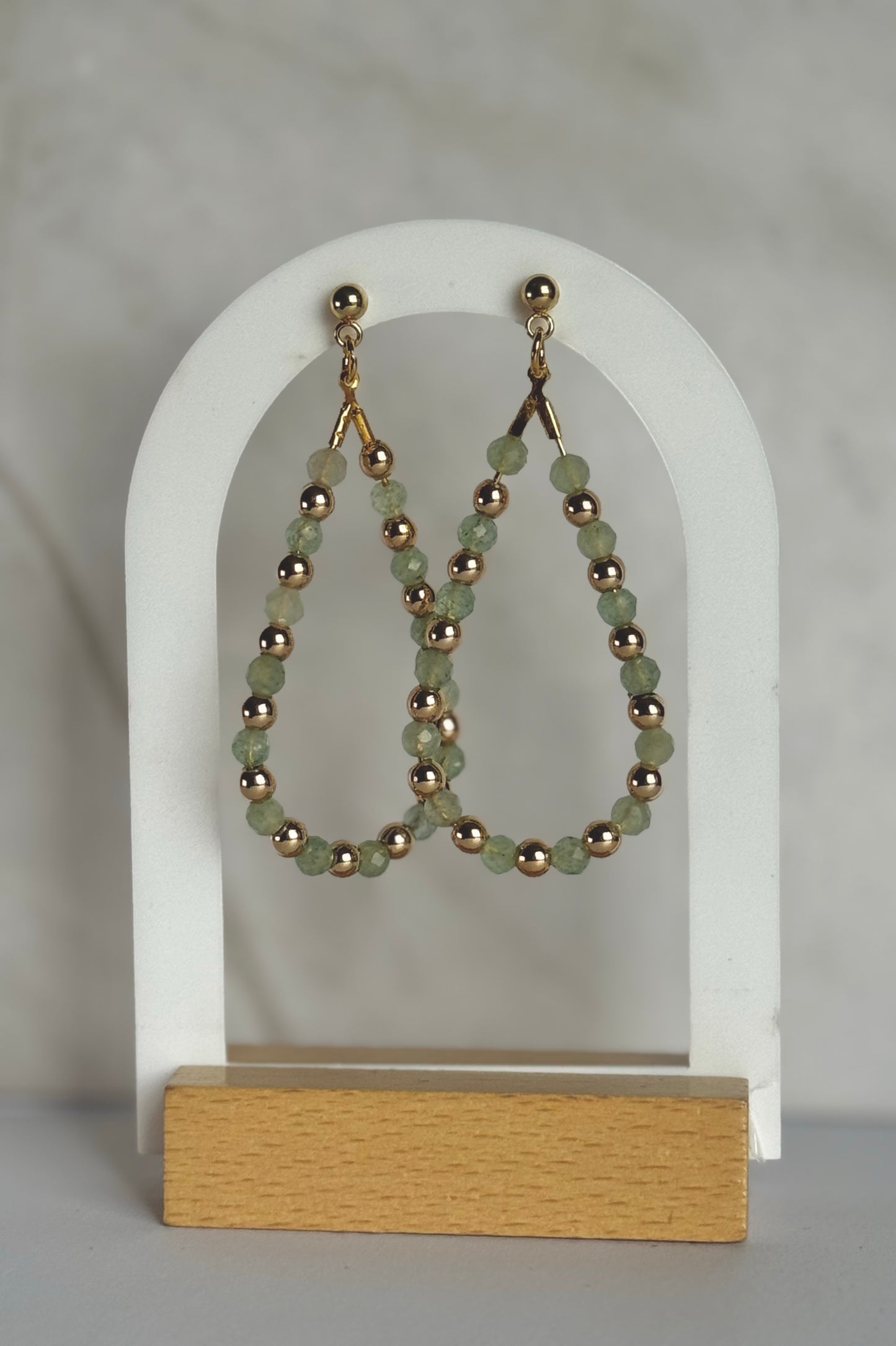 Beaded earrings on a white arch with a wooden base against a gray background