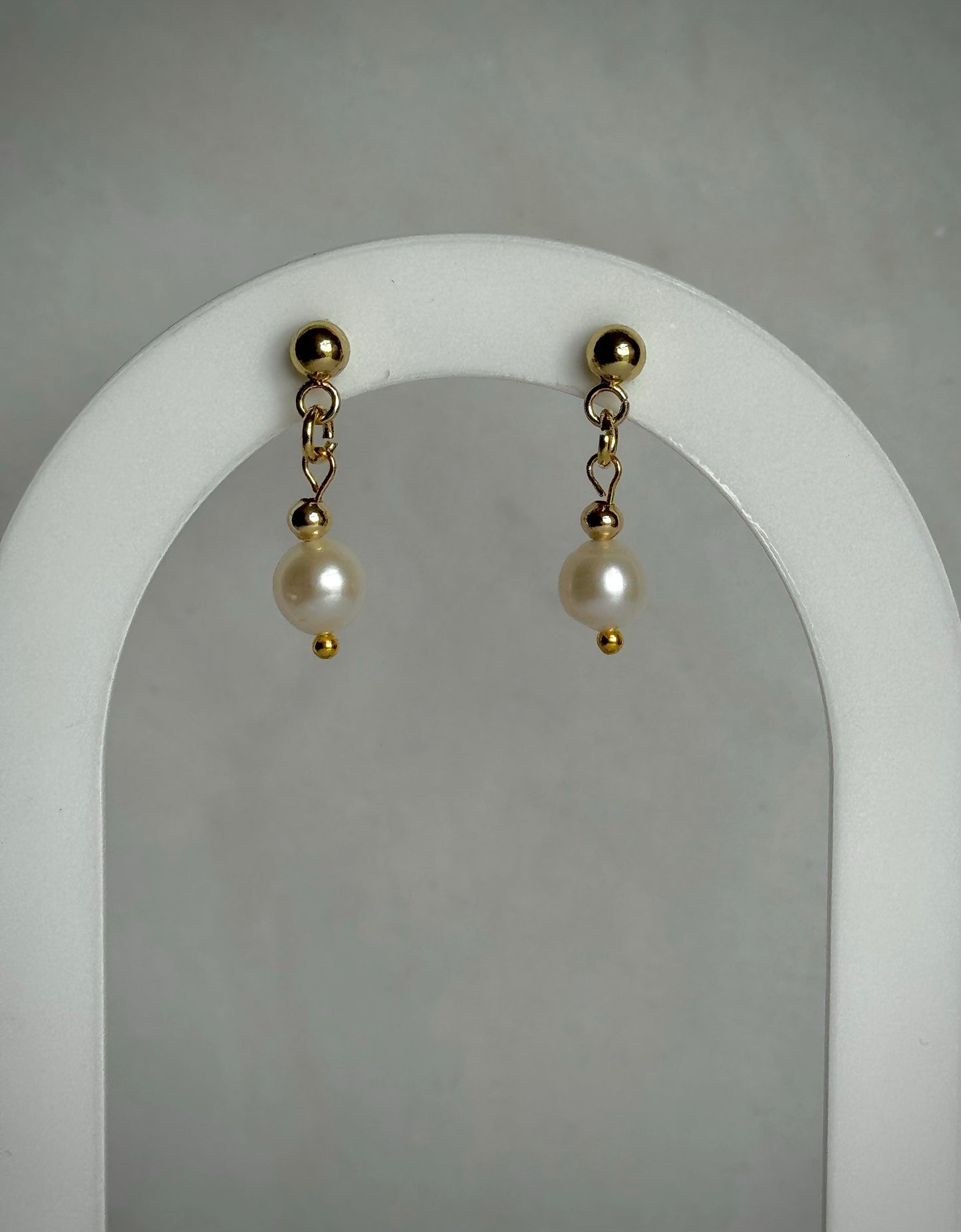 Pair of pearl earrings with gold accents on a white earring display archway.