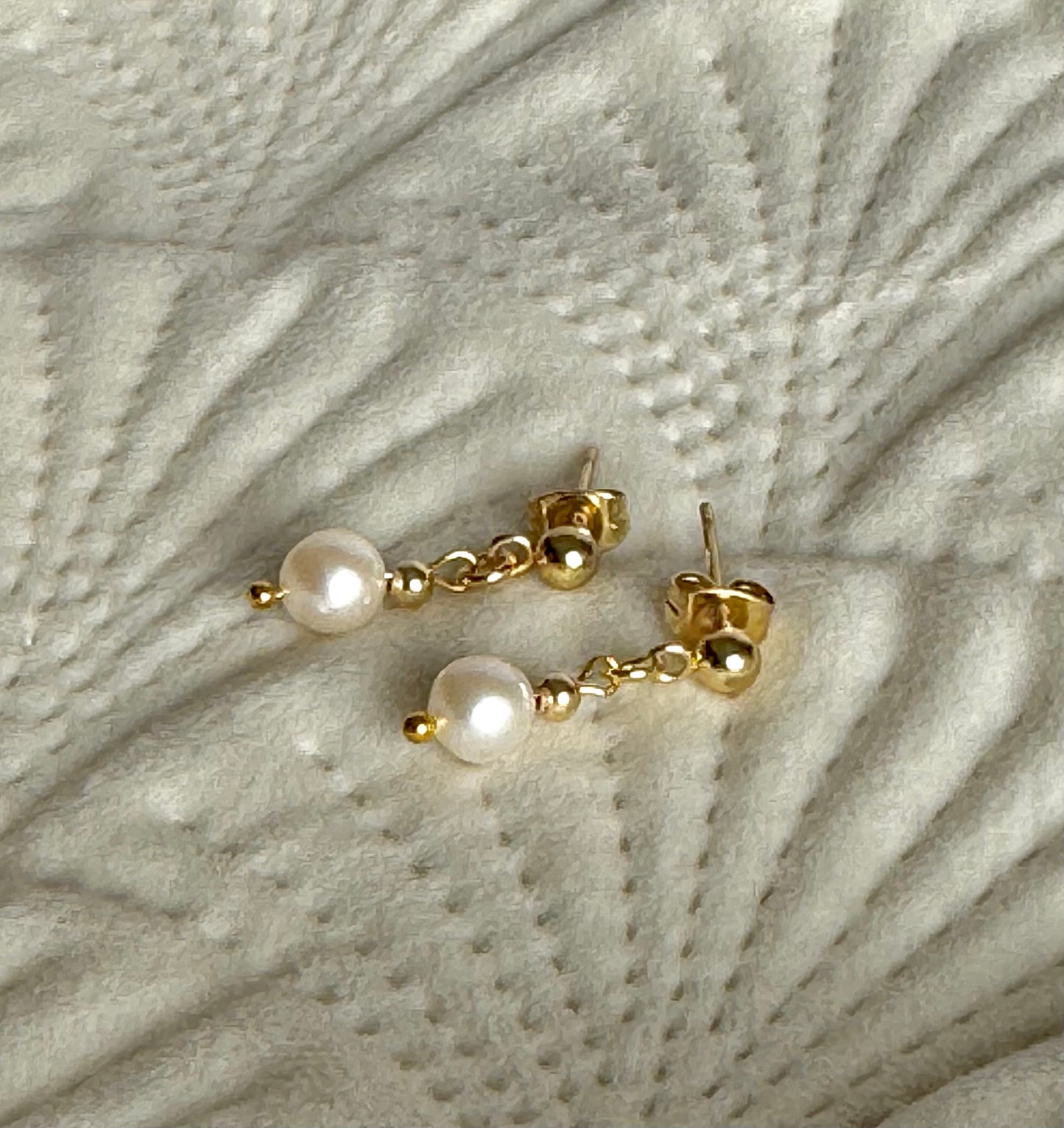 Gold earrings with pearls on a textured grey surface