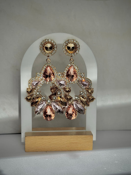Elegant earrings with pink and gold stones on a white arch and wooden base.