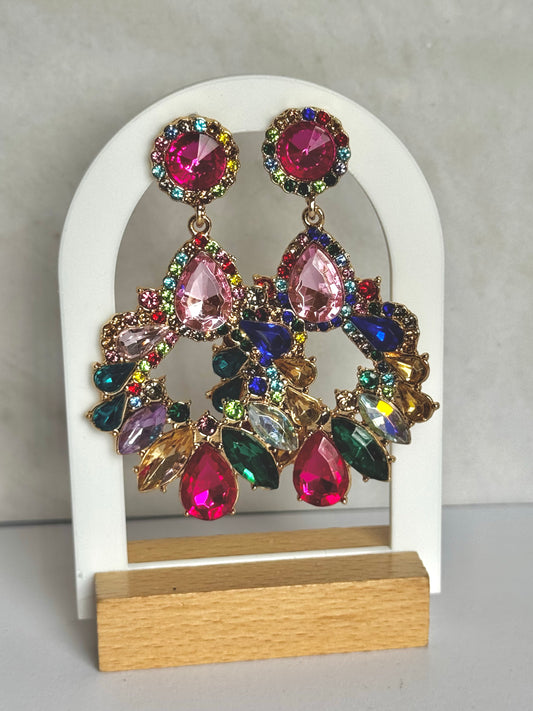 Multi-coloured gemstone earrings on a white and wooden stand against a grey background