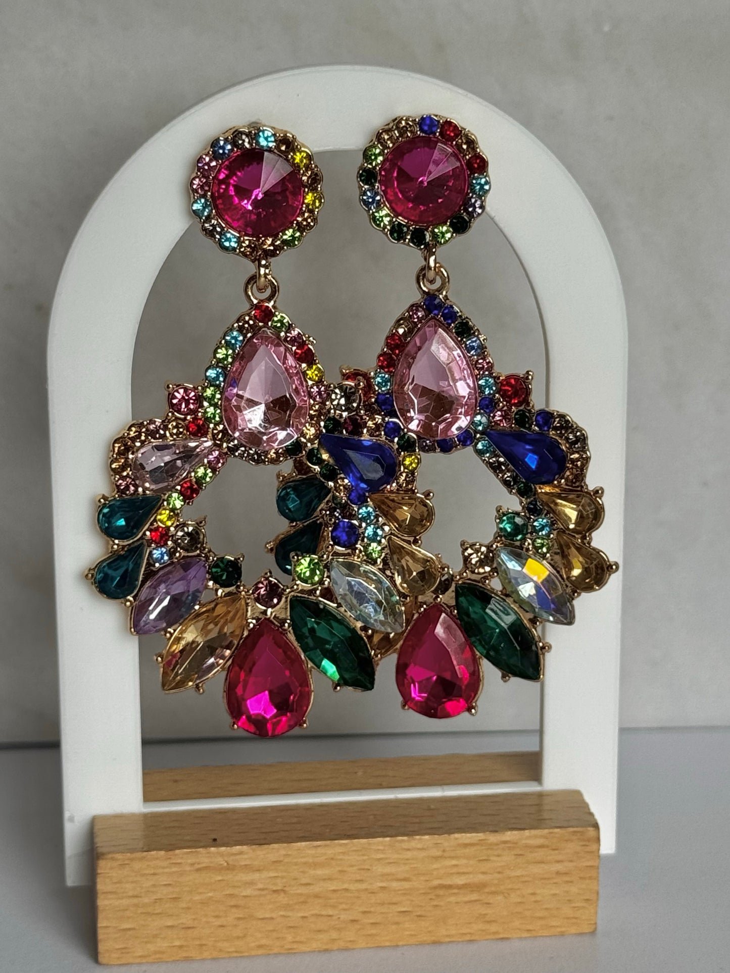 Colourful gemstone earrings on a white arch stand with a grey background