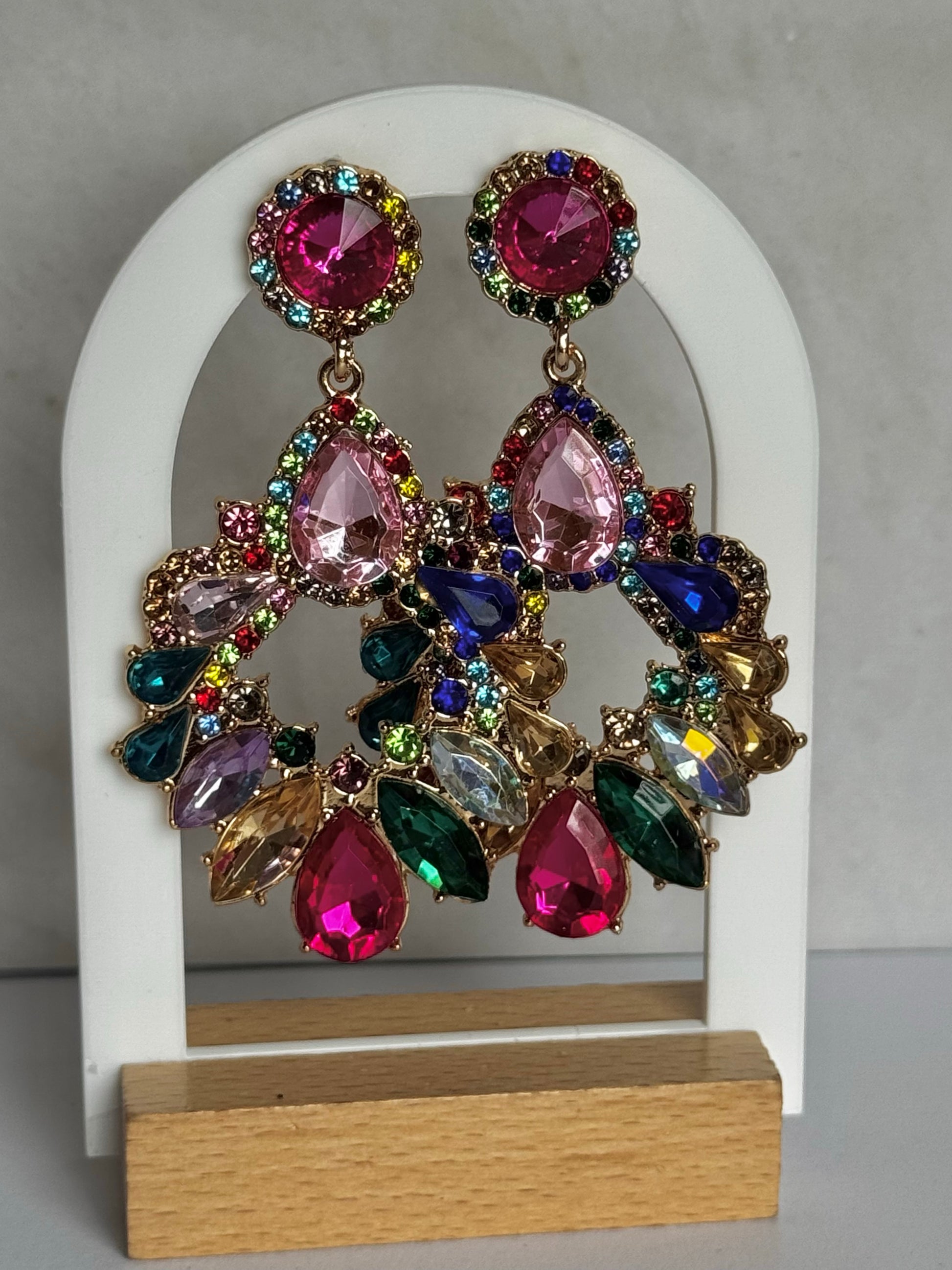Colourful gemstone earrings on a white arch stand with a grey background