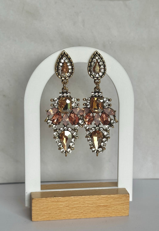 Pair of ornate earrings on a white arch stand with a grey background