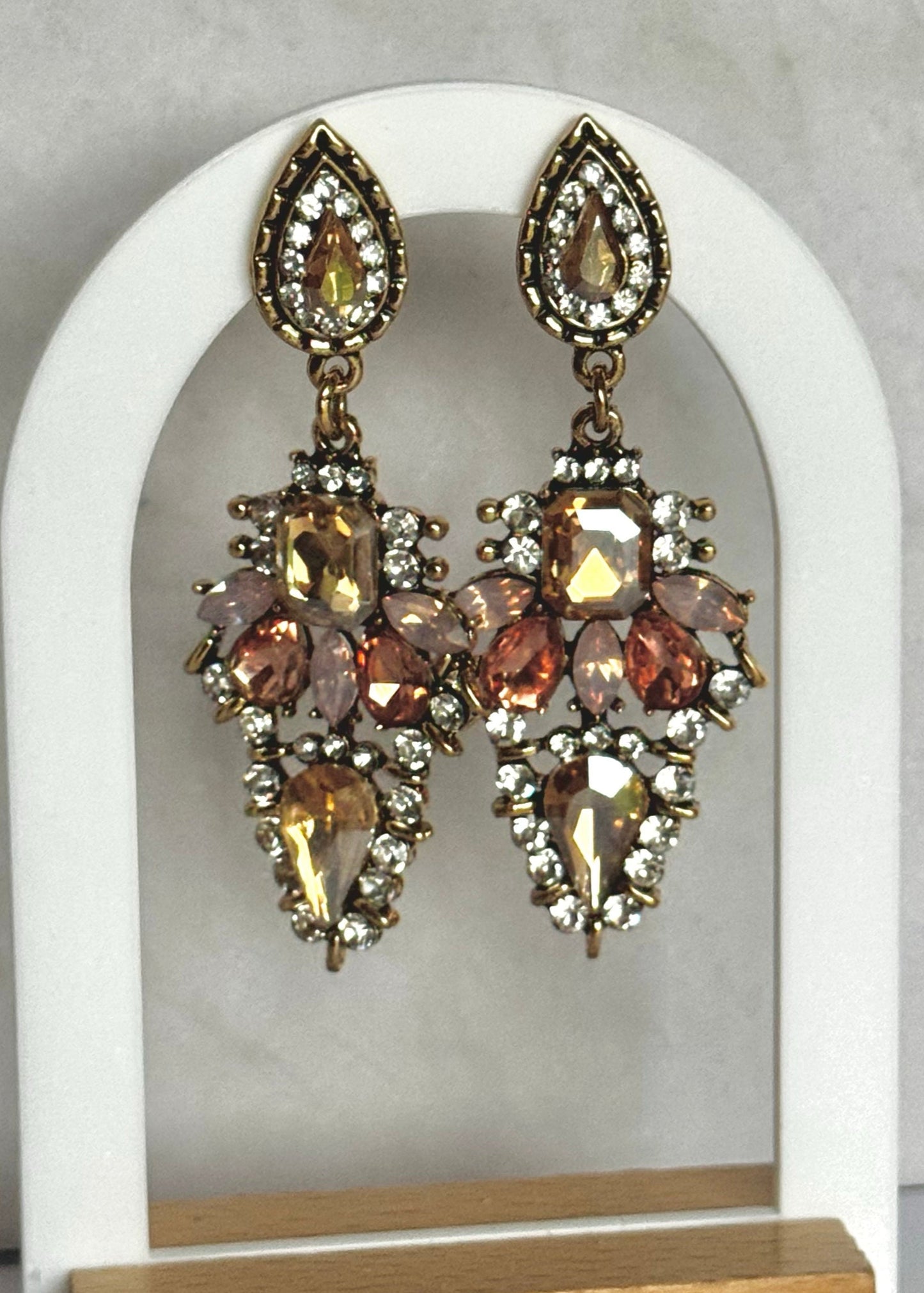 Pair of crystal champagne coloured earrings on a white arch display stand with a wooden base.