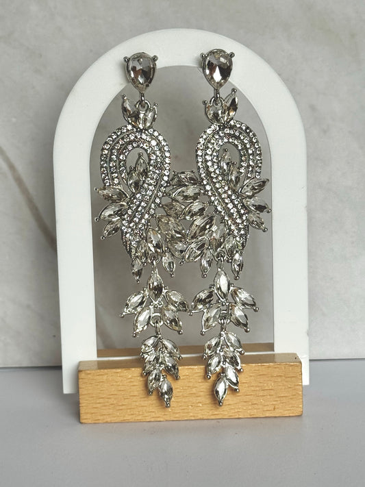 Silver bridal earrings on a wooden stand with a white arch background