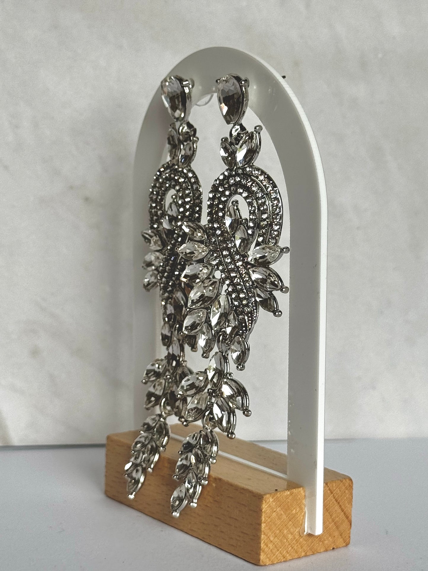 Silver bridal earrings on a white arch stand against a grey background