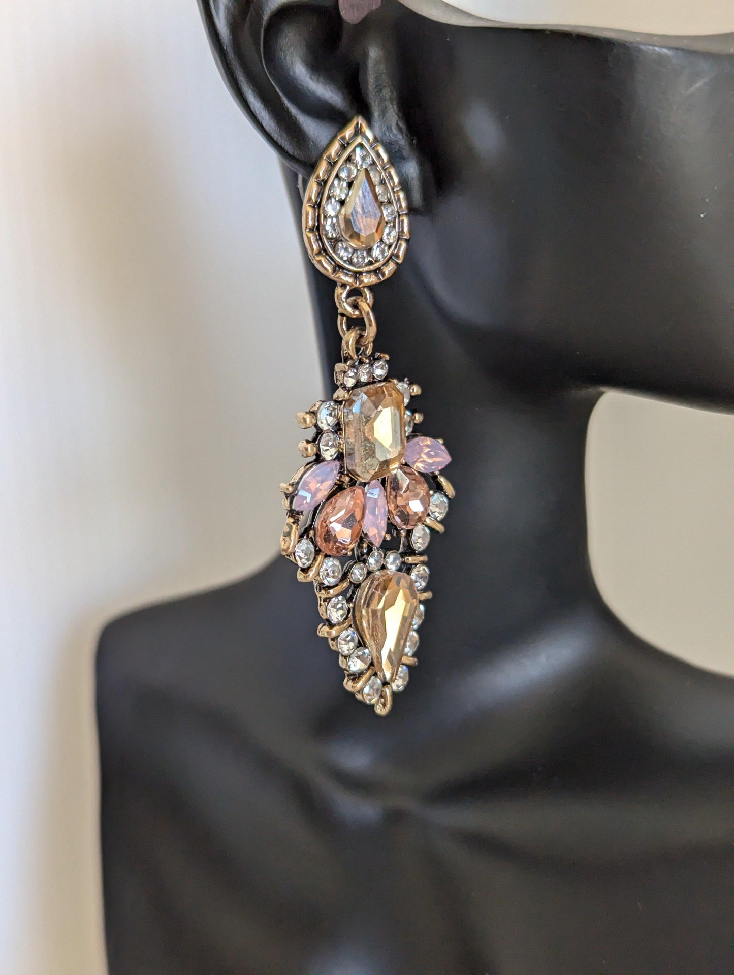 vintage-inspired crystal drop earrings, featuring a rich mix of champagne and blush pink gemstones displayed on a black earring model prop