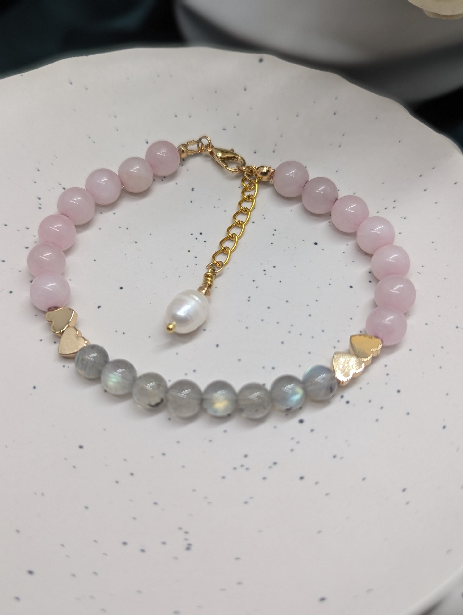 Top view of a crystal beaded bracelet made with natural rose quartz and labradorite, gold-plated heart spacers, and a single freshwater pearl charm