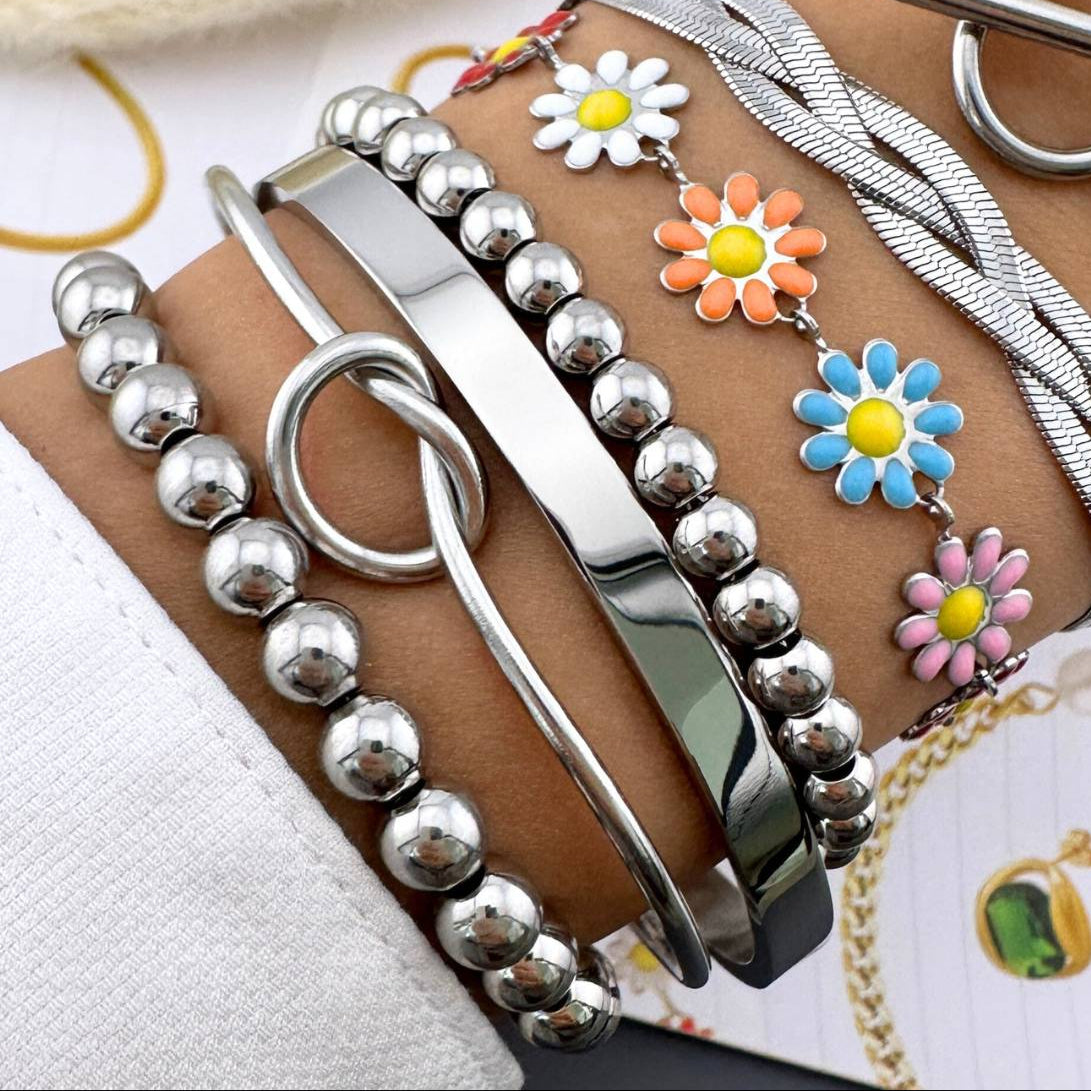 Stack of waterproof stainless steel bracelets and colourful daisy enamel chain on wrist – hypoallergenic, tarnish-free jewellery for women