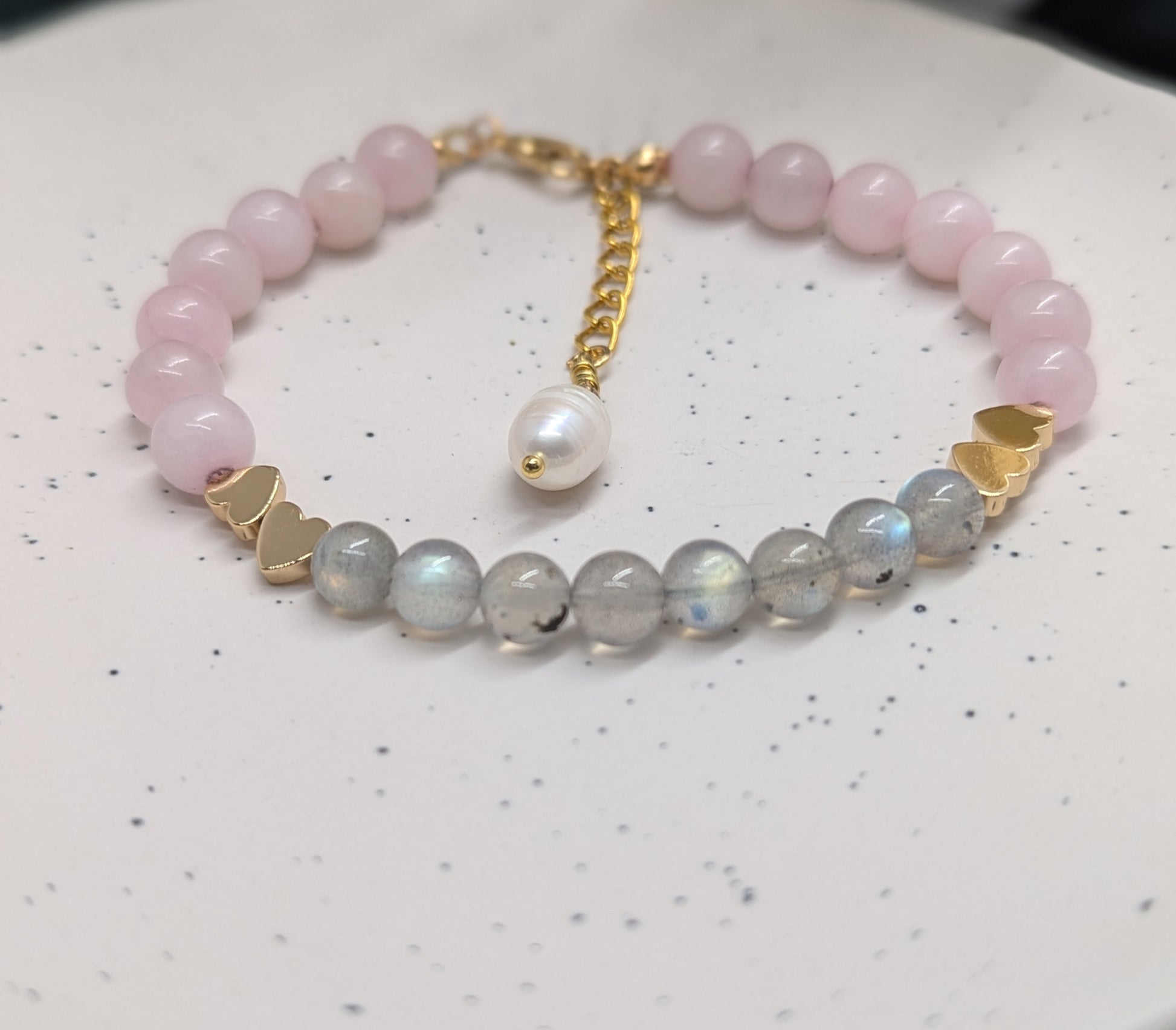 Top view of a crystal beaded bracelet made with natural rose quartz and labradorite, gold-plated heart spacers, and a single freshwater pearl charm