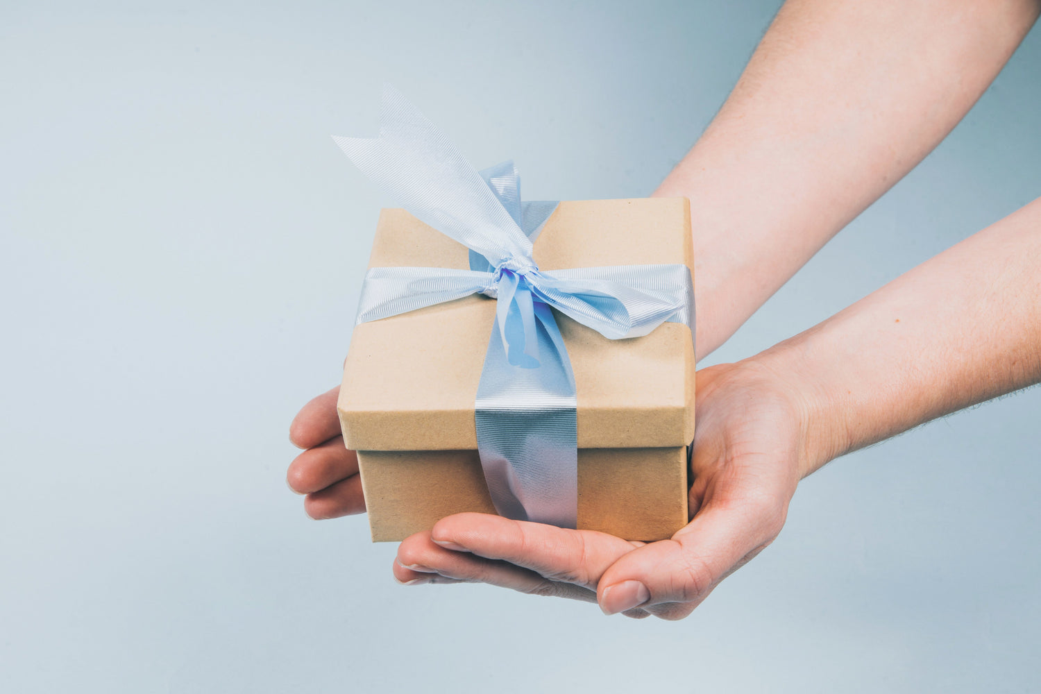 a pair of hands holding a gift box with a blue ribbon.  Gift giving.