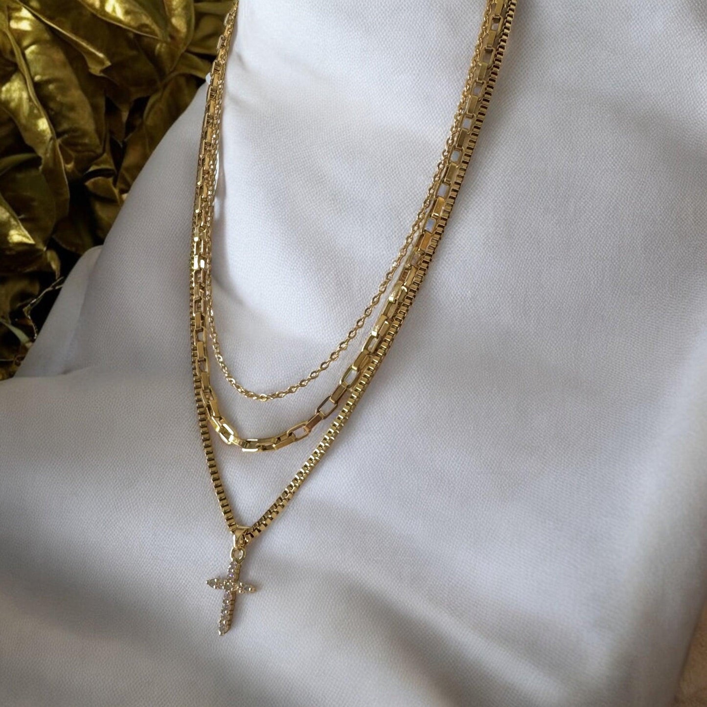 Side view of 18K gold layered necklace with cross pendant – features three waterproof and tarnish-resistant chain styles, displayed on white stand"