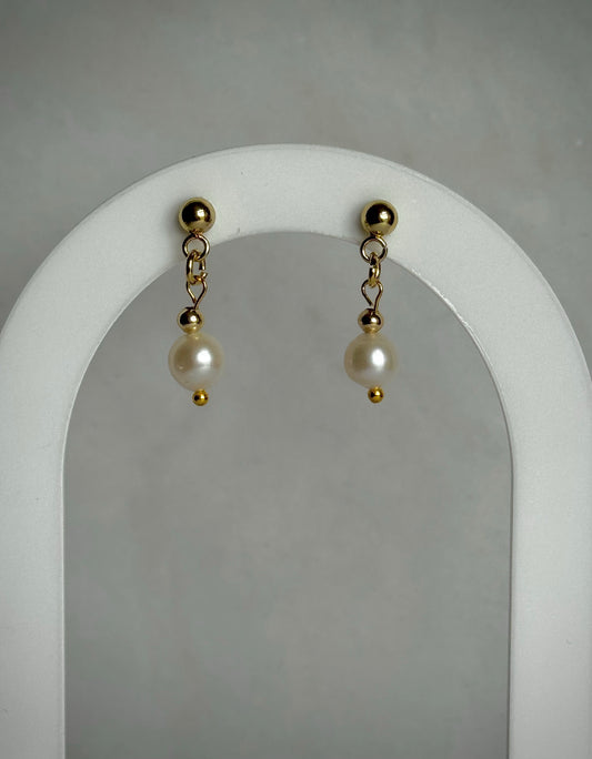 Pair of pearl earrings with gold accents on a white earring display archway.