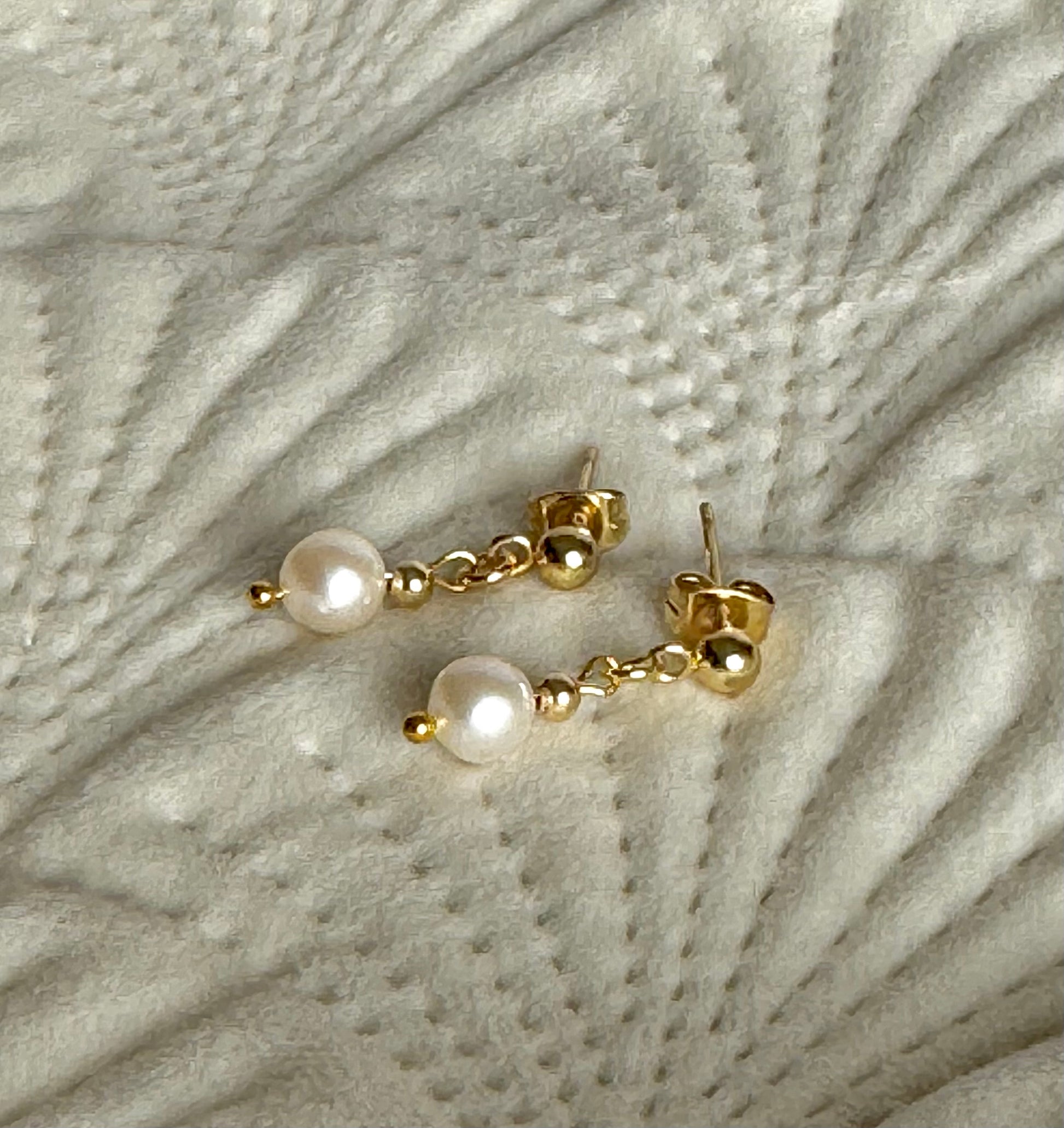 Gold earrings with pearls on a textured grey surface
