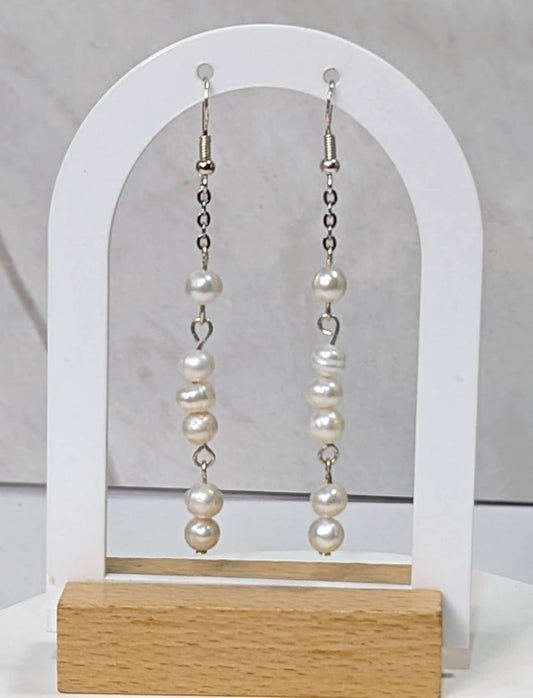 Romantic white pearl drop earrings in sterling silver, silver ear wires hanging from a earring stand